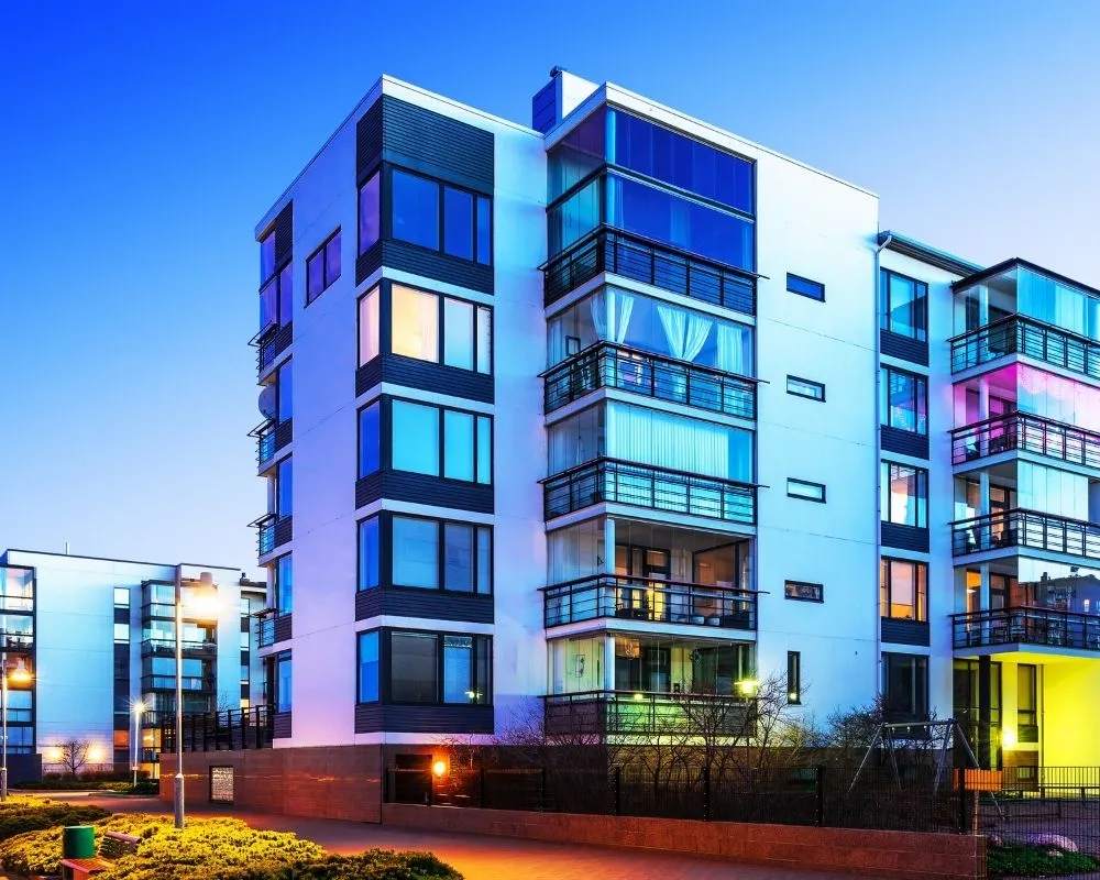 Modern apartment building with glass balconies and lit windows photographed at twilight