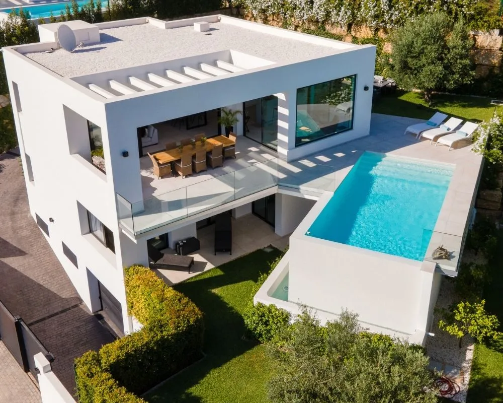 Aerial drone view of a modern white home with a covered dining terrace, pool deck and swimming pool